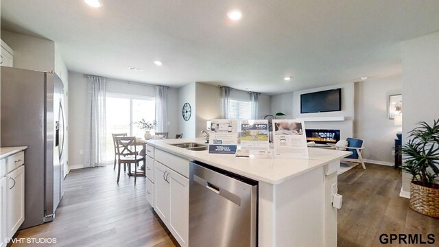 kitchen with white cabinets, stainless steel appliances, hardwood / wood-style flooring, and a center island with sink