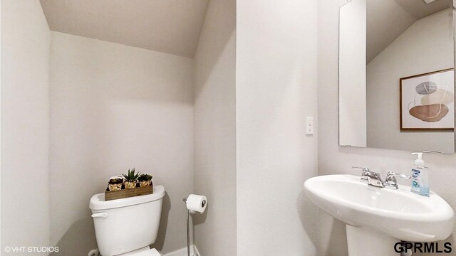 bathroom featuring toilet, sink, and lofted ceiling