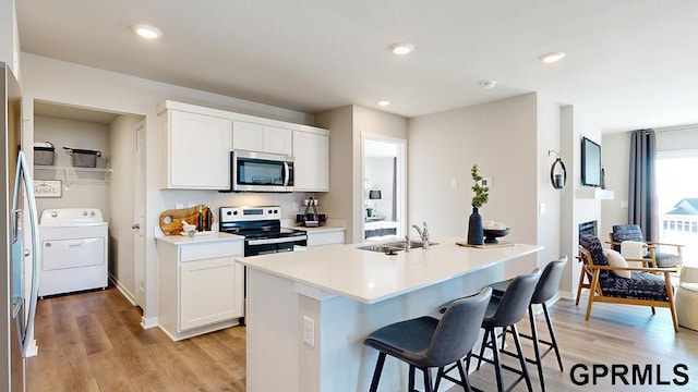 kitchen featuring sink, appliances with stainless steel finishes, an island with sink, white cabinets, and washer / dryer