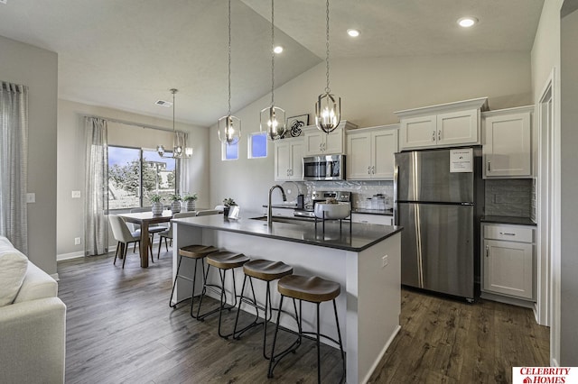 kitchen featuring stainless steel appliances, a sink, white cabinetry, dark countertops, and a kitchen bar