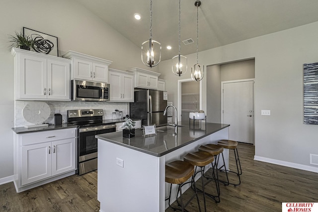 kitchen with appliances with stainless steel finishes, dark countertops, white cabinetry, and a center island with sink