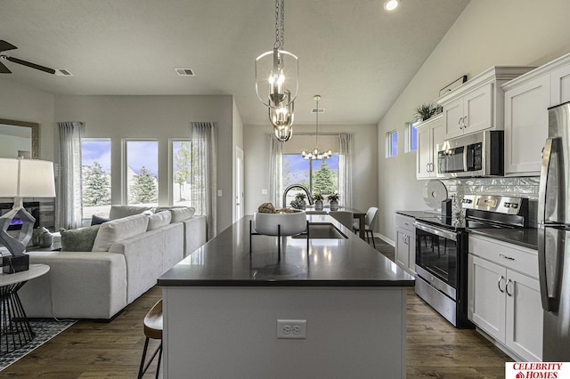 kitchen with open floor plan, stainless steel appliances, an island with sink, and dark countertops