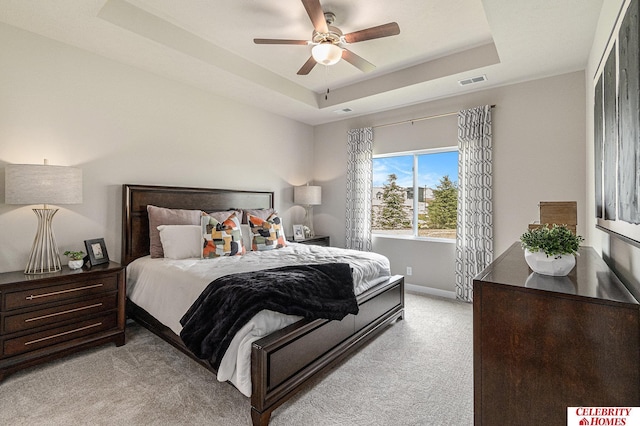 bedroom featuring a tray ceiling, visible vents, a ceiling fan, light carpet, and baseboards