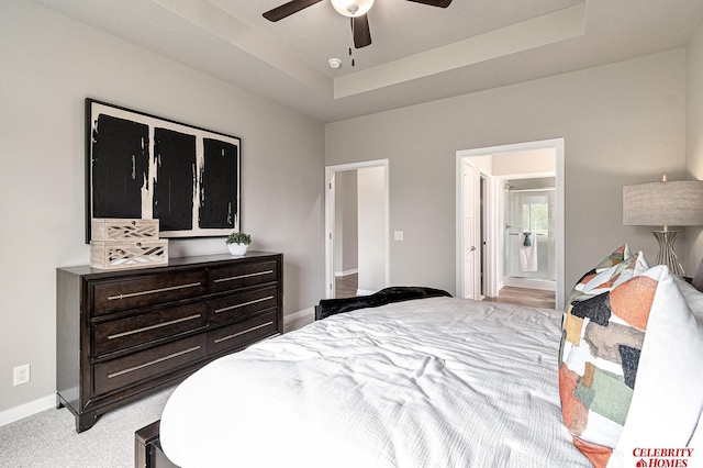 bedroom with a tray ceiling, a ceiling fan, light carpet, ensuite bath, and baseboards