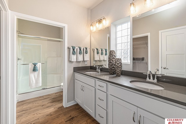 bathroom with double vanity, wood finished floors, a sink, and a shower stall