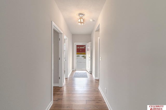 hallway with a textured ceiling, wood finished floors, and baseboards