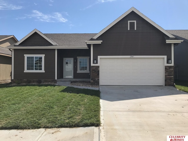 view of front of home featuring a shingled roof, an attached garage, a front yard, stone siding, and driveway