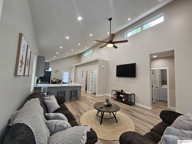 living room featuring separate washer and dryer, a towering ceiling, sink, and light wood-type flooring