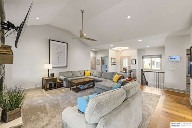 living room with ceiling fan, a stone fireplace, vaulted ceiling, and light wood-type flooring