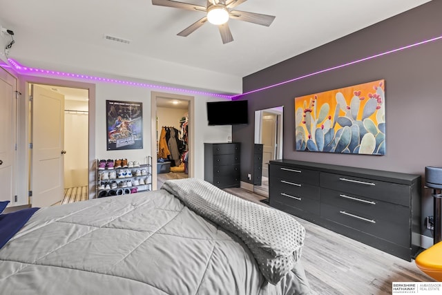 bedroom with ceiling fan, a walk in closet, a closet, and light hardwood / wood-style flooring