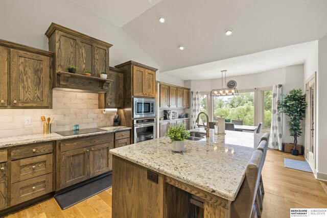 kitchen featuring light wood-type flooring, vaulted ceiling, stainless steel appliances, and an island with sink