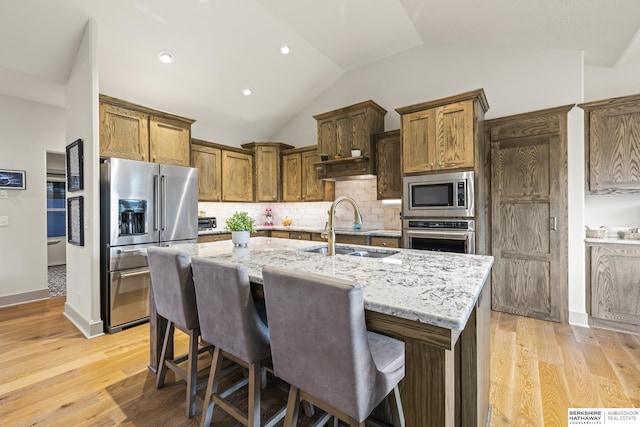 kitchen with sink, a breakfast bar area, a kitchen island with sink, stainless steel appliances, and light stone counters