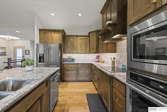 kitchen featuring light stone countertops, backsplash, light hardwood / wood-style flooring, and stainless steel appliances