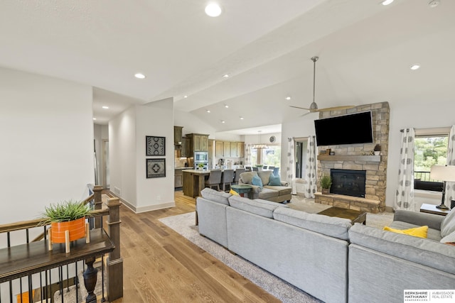 living room with a stone fireplace, lofted ceiling with beams, ceiling fan, and light wood-type flooring