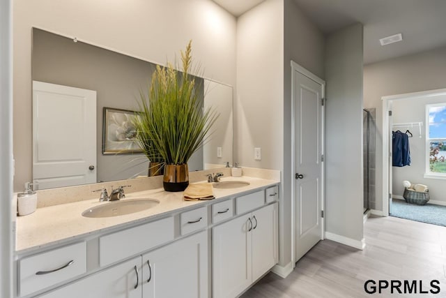 full bathroom featuring a stall shower, a sink, baseboards, and double vanity