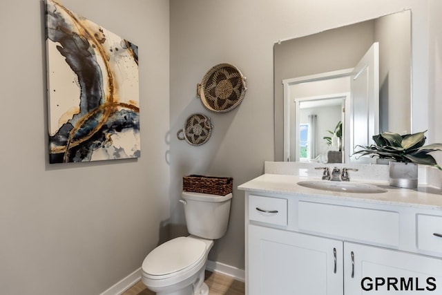 half bathroom featuring toilet, baseboards, and vanity