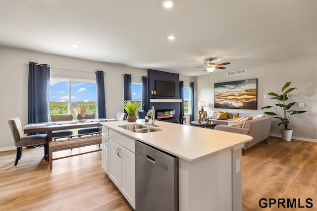 kitchen with light wood-style flooring, a kitchen island with sink, a sink, white cabinetry, and stainless steel dishwasher