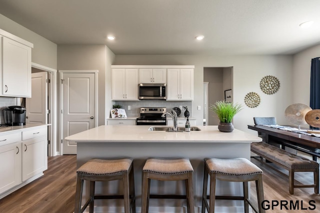 kitchen featuring stainless steel appliances, a sink, white cabinets, decorative backsplash, and a kitchen bar