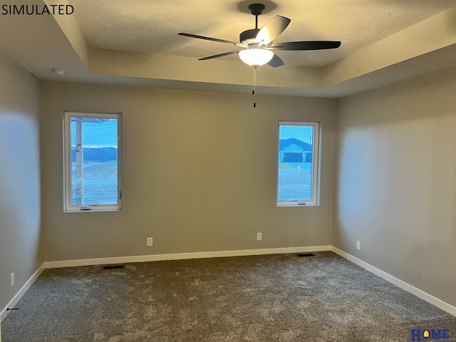 unfurnished room with ceiling fan, a raised ceiling, carpet floors, and plenty of natural light