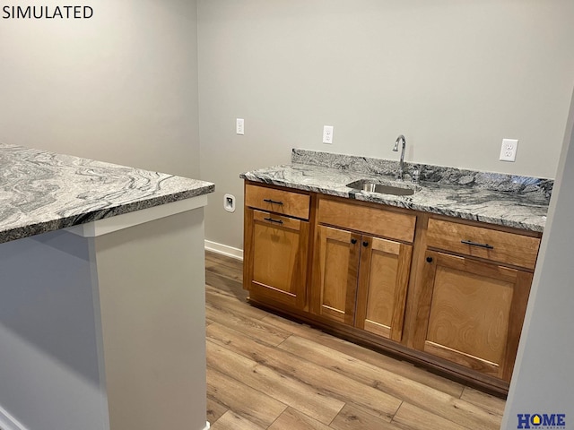 kitchen with sink, light hardwood / wood-style flooring, and light stone counters