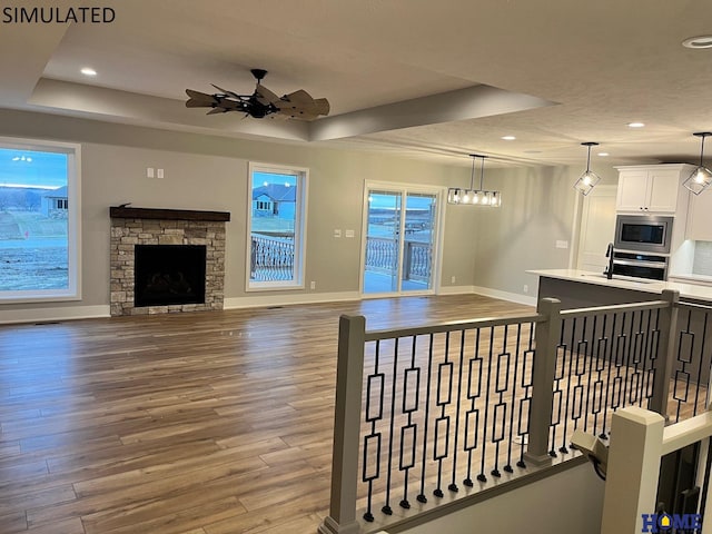 living room featuring a tray ceiling, ceiling fan, hardwood / wood-style flooring, and a fireplace