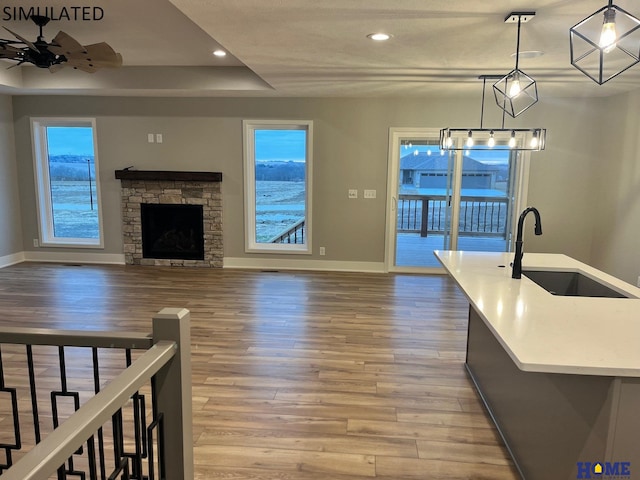 interior space with sink, light wood-type flooring, ceiling fan, and a stone fireplace