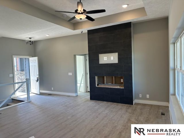 unfurnished living room featuring ceiling fan, wood-type flooring, a tile fireplace, and a wealth of natural light