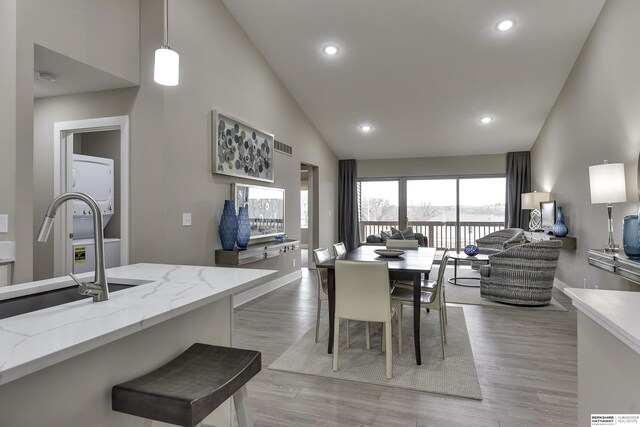 dining area with sink, high vaulted ceiling, light wood-type flooring, and stacked washer / dryer