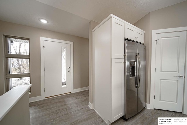 kitchen with white cabinetry, a textured ceiling, wood finished floors, stainless steel fridge, and baseboards