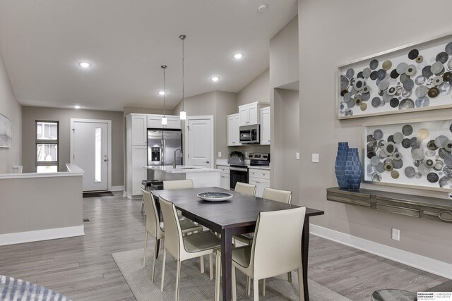 dining room with sink, light hardwood / wood-style floors, and vaulted ceiling