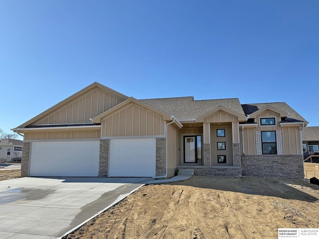 view of front of property featuring roof with shingles, board and batten siding, a garage, stone siding, and driveway