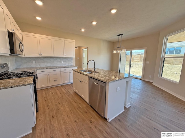 kitchen featuring backsplash, light stone counters, light wood-style floors, stainless steel appliances, and a sink