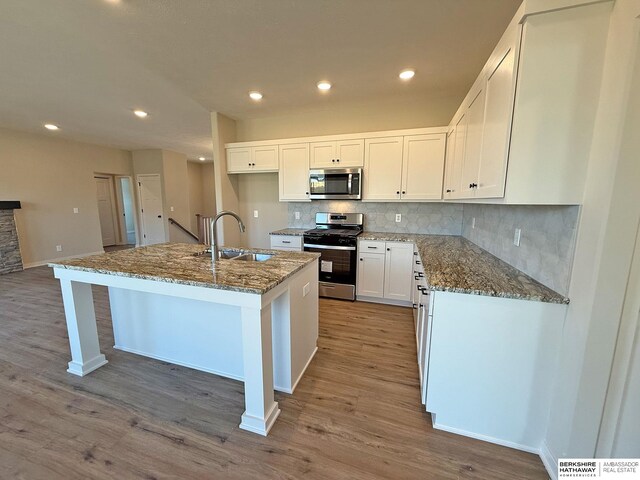 kitchen with wood finished floors, appliances with stainless steel finishes, dark stone counters, and a sink