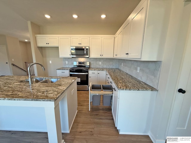 kitchen with dark stone countertops, appliances with stainless steel finishes, wood finished floors, white cabinets, and a sink