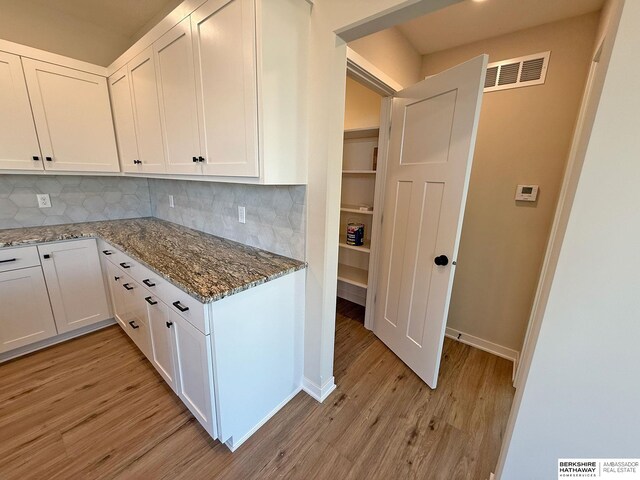 kitchen featuring light wood-style flooring, light stone countertops, visible vents, and white cabinets