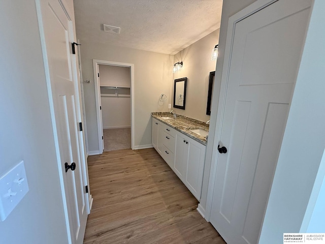 full bath featuring visible vents, double vanity, wood finished floors, a textured ceiling, and a sink