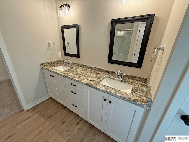 bathroom featuring double vanity, wood finished floors, baseboards, and a sink