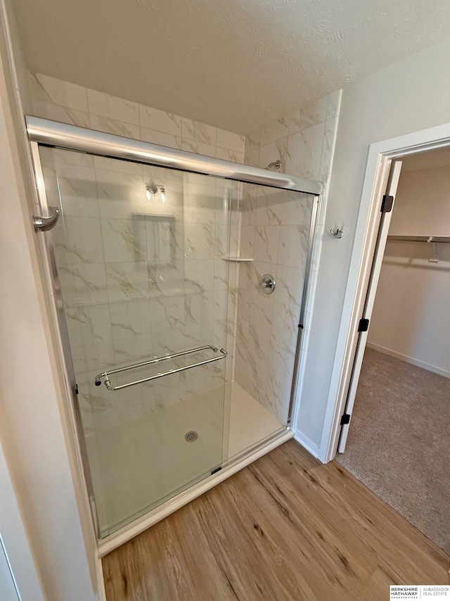 bathroom featuring a marble finish shower, a walk in closet, baseboards, wood finished floors, and a textured ceiling