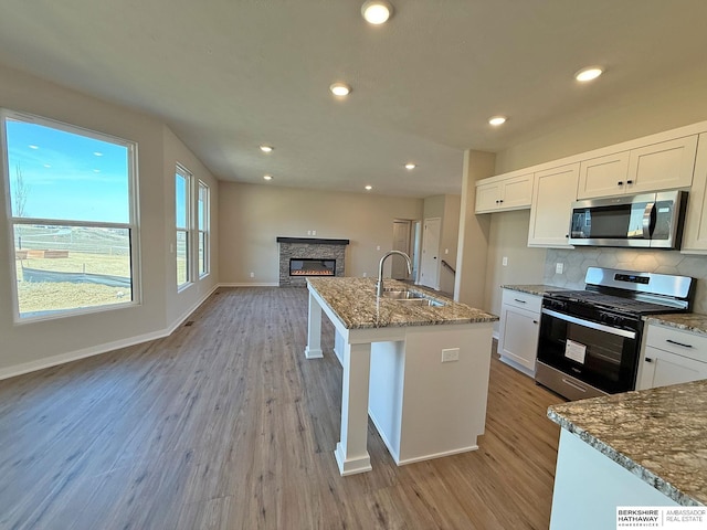 kitchen featuring a sink, dark stone countertops, open floor plan, stainless steel appliances, and a fireplace