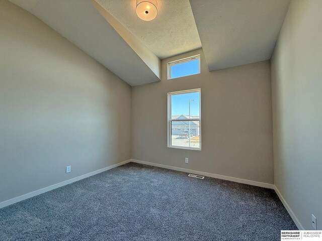 empty room featuring visible vents, baseboards, dark carpet, vaulted ceiling, and a textured ceiling