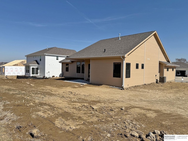 back of house featuring cooling unit and roof with shingles