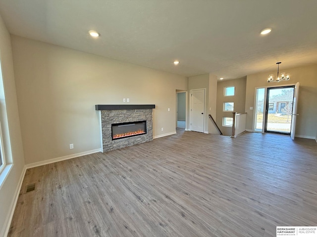 unfurnished living room with a chandelier, a fireplace, baseboards, and wood finished floors