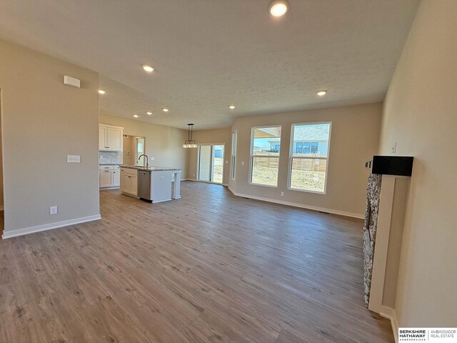 unfurnished living room with recessed lighting, baseboards, wood finished floors, and a sink