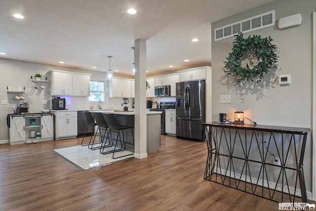 kitchen with appliances with stainless steel finishes, hanging light fixtures, light countertops, a kitchen bar, and white cabinetry