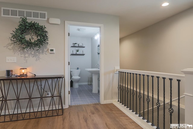 corridor with baseboards, visible vents, wood finished floors, an upstairs landing, and a sink