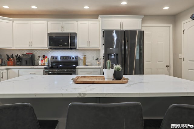 kitchen with white cabinetry, stainless steel appliances, light stone counters, and a kitchen breakfast bar