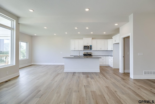 kitchen featuring decorative backsplash, light hardwood / wood-style flooring, an island with sink, white cabinets, and stove