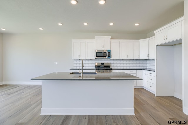 kitchen featuring a kitchen island with sink, sink, stove, and white cabinets