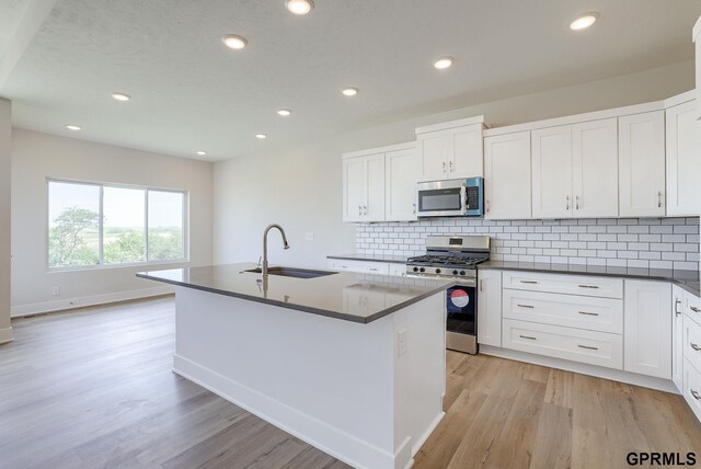 kitchen with a kitchen island with sink, sink, stainless steel appliances, and light wood-type flooring