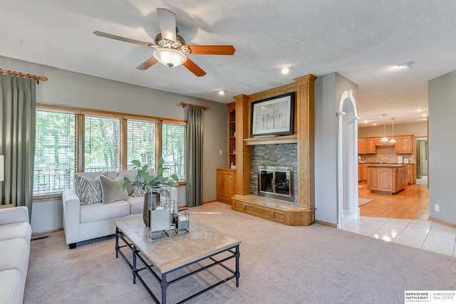 living room with a fireplace, light colored carpet, sink, ceiling fan, and a textured ceiling